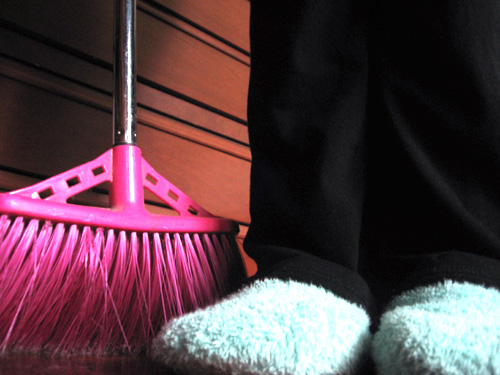a broom with a pink handle being placed next to another pair of feet