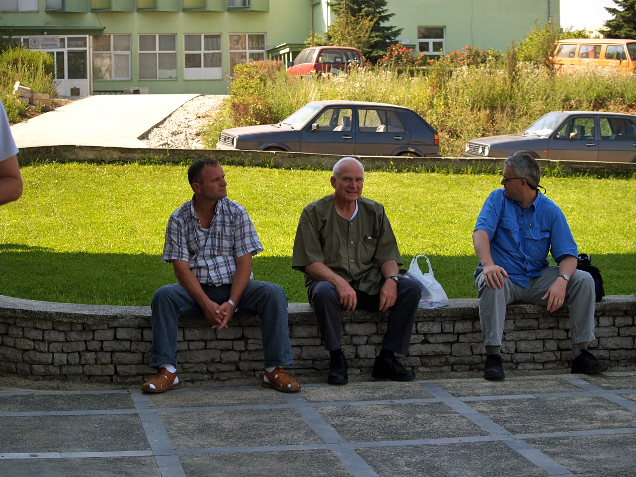 four men sitting on the side walk with bags and a car in background