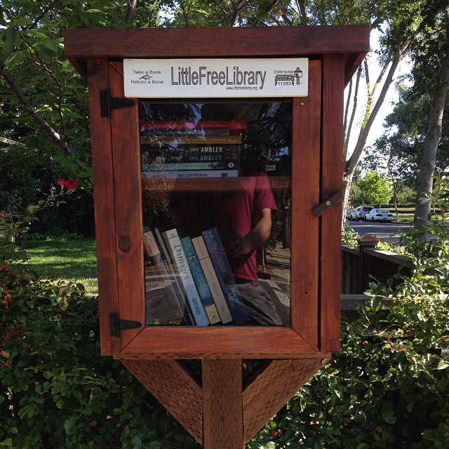 a wooden display with books on it by bushes
