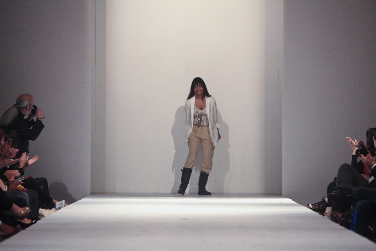 a woman stands in the middle of a runway wearing a coat