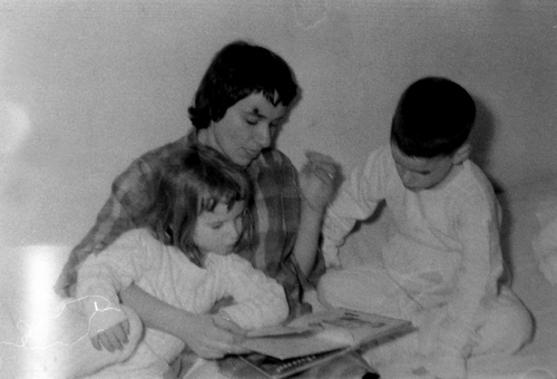 two children sit on a bed with their mother reading