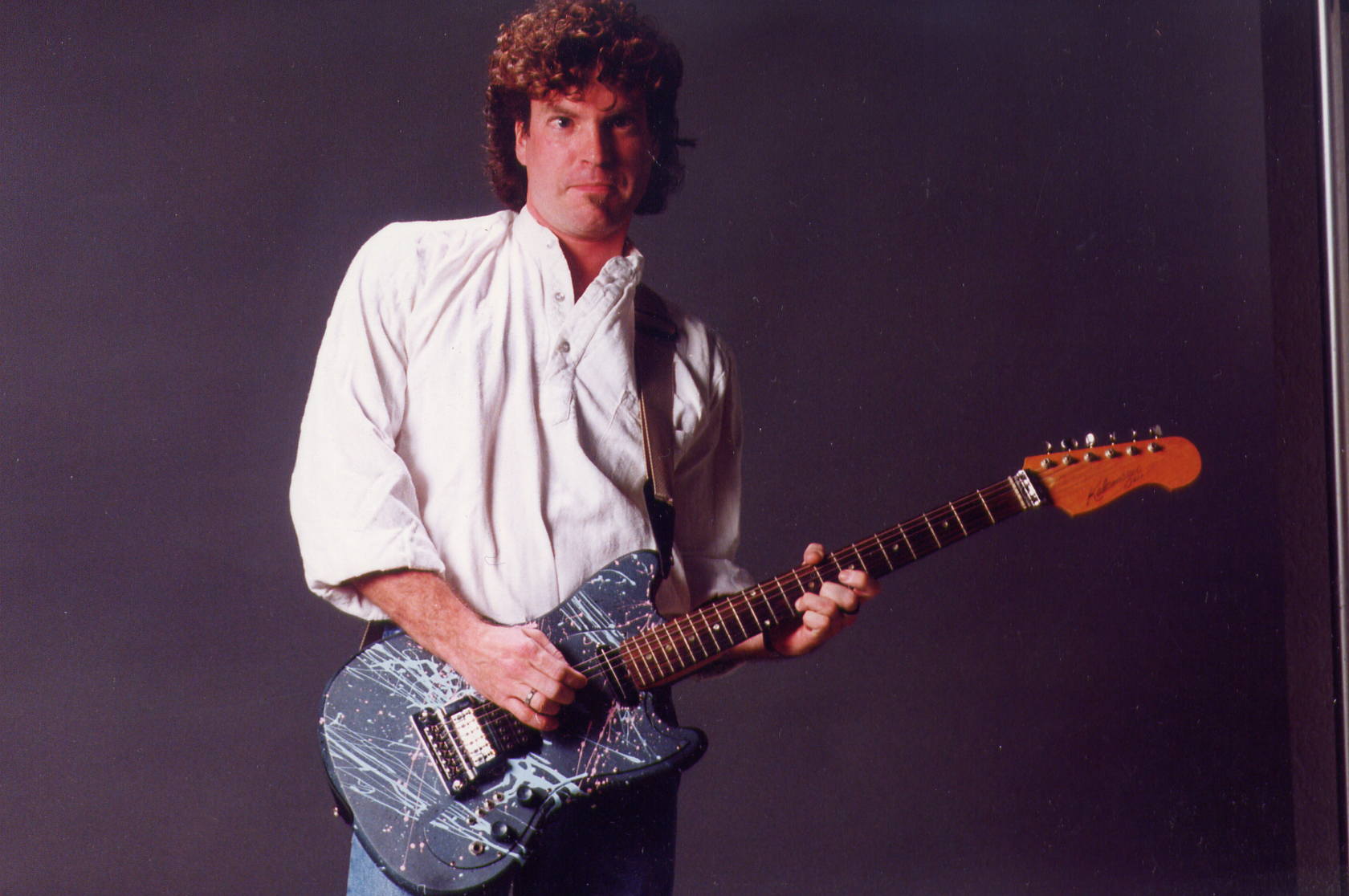 a man holding a guitar standing in front of a gray background