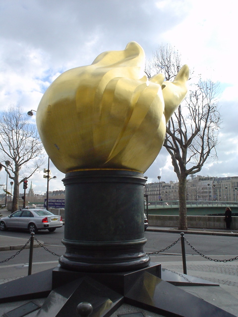 a yellow sculpture on a pedestal in front of cars