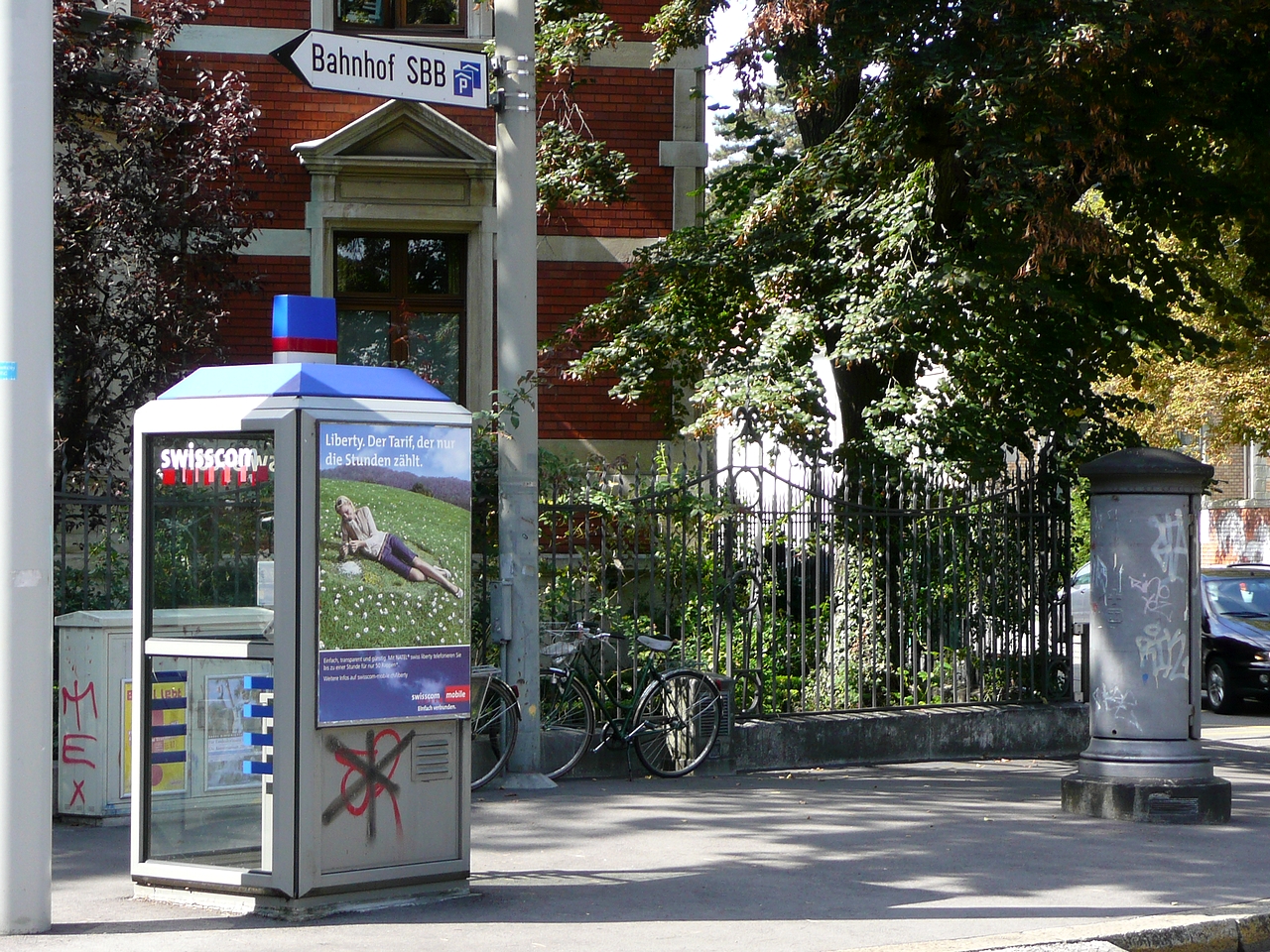 two public telephone booths along the sidewalk next to trees