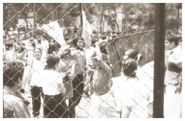 black and white po of man holding signs behind a chain link fence