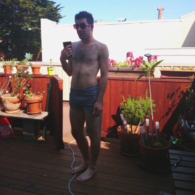 the shirtless man stands on his deck with his hands in his pockets