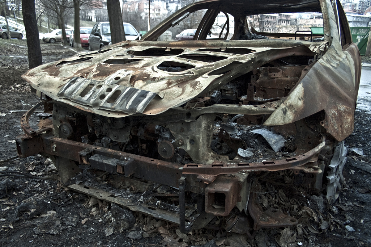 a burnt car in a forest with several trees behind it