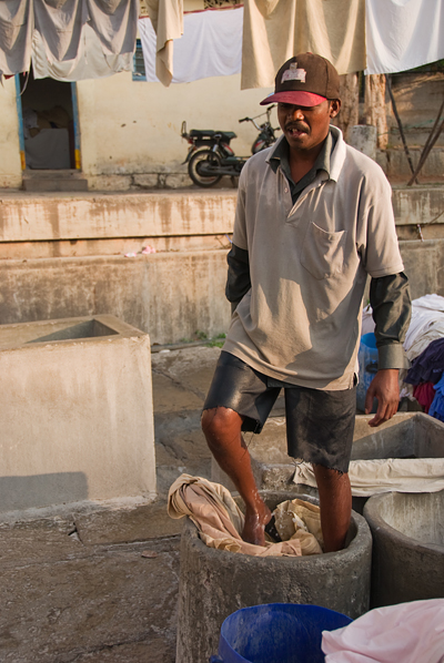 man standing in dirty area with blue buckets and other objects