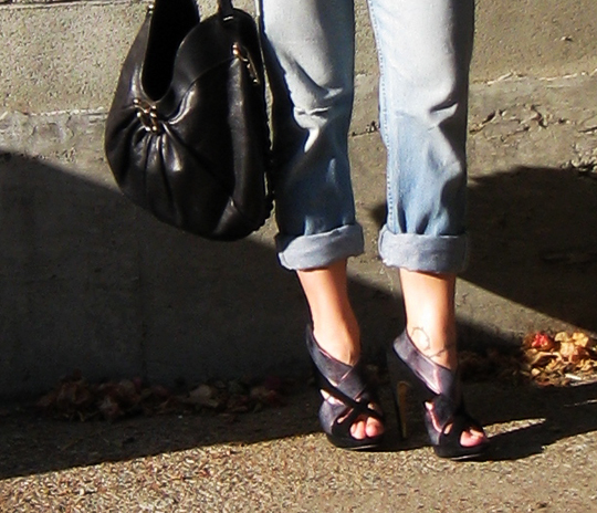 a person wearing high heels and jeans is holding a handbag