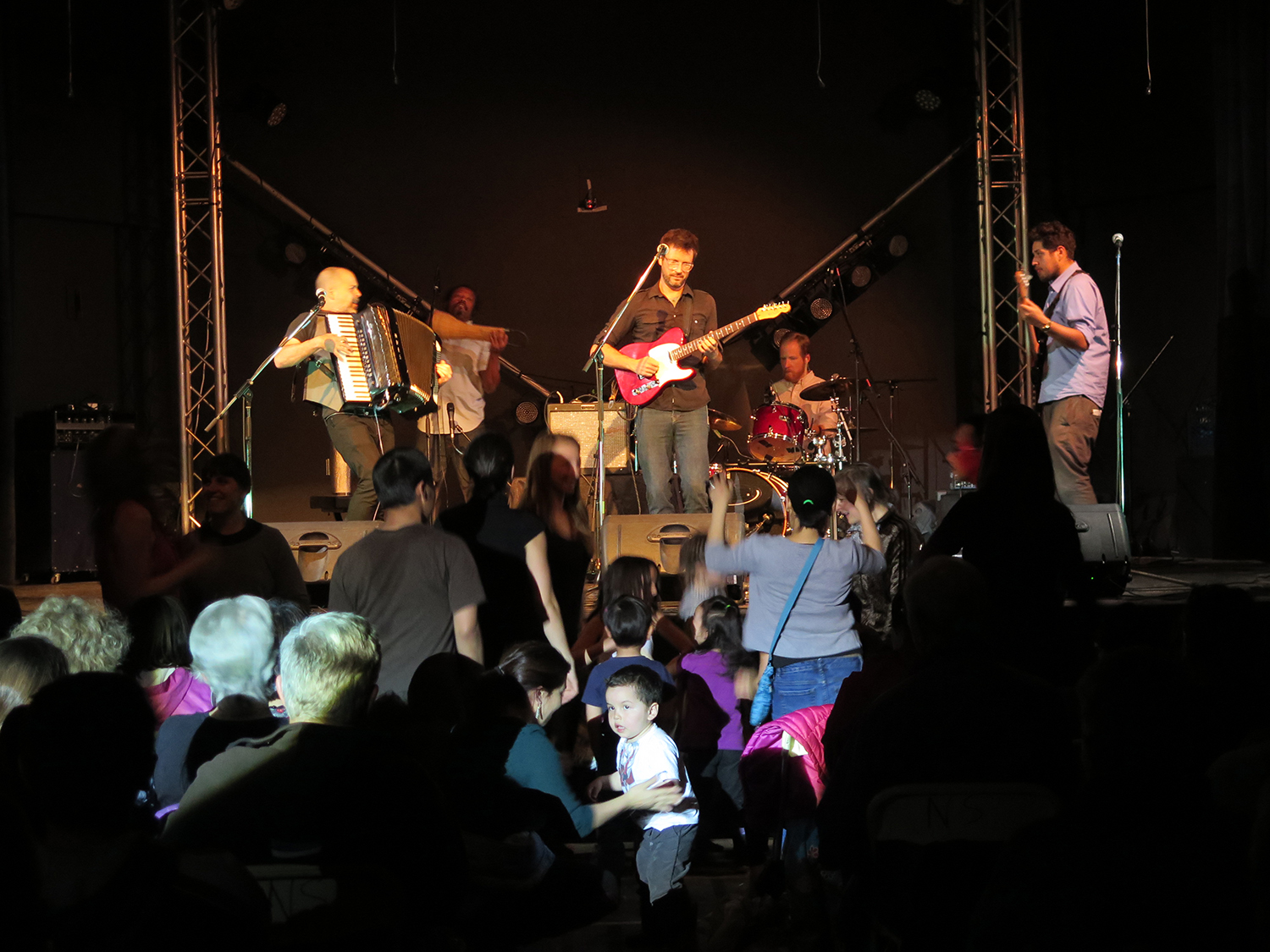 three men are singing on stage with lots of spectators