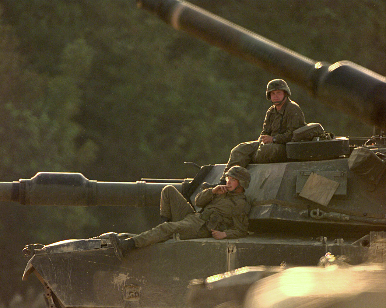 two soldiers relaxing on top of tank in field