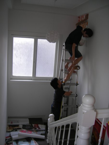 man climbing up the wall, holding on to a ladder, and standing next to another guy as they climb up a stairwell