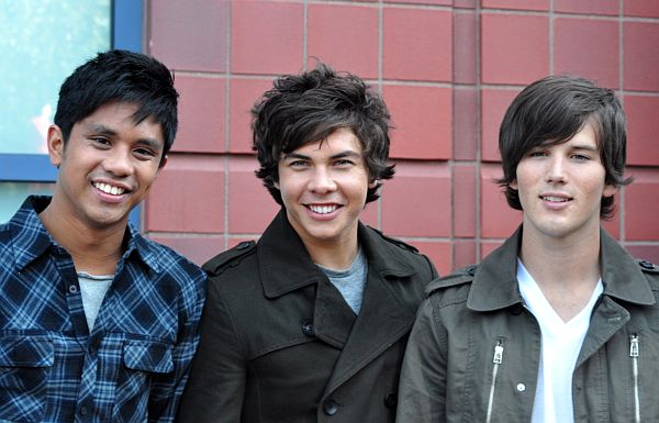 four young men smiling together in front of a red brick building