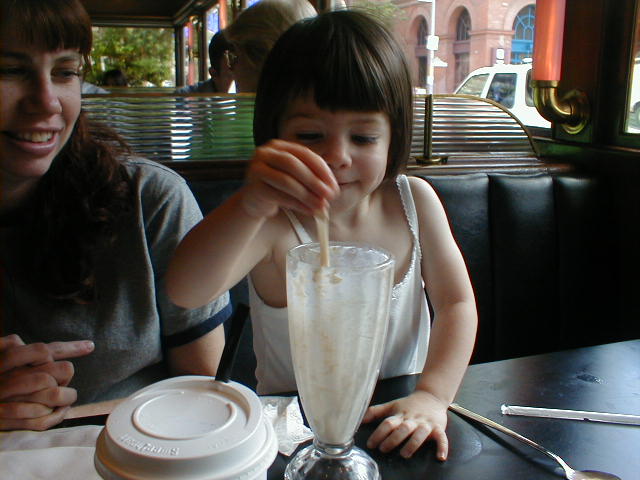 a little girl sitting at a table in front of a blender