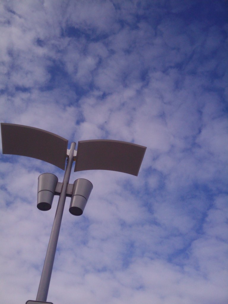 two metal lights attached to a pole and some white clouds