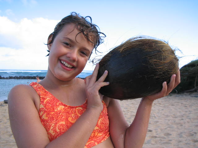 girl smiling holding a giant coconut on the beach