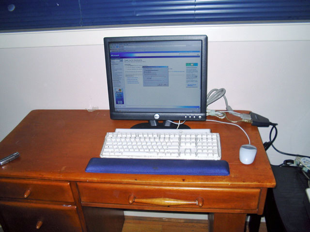 a small wooden desk with a computer monitor, keyboard and mouse