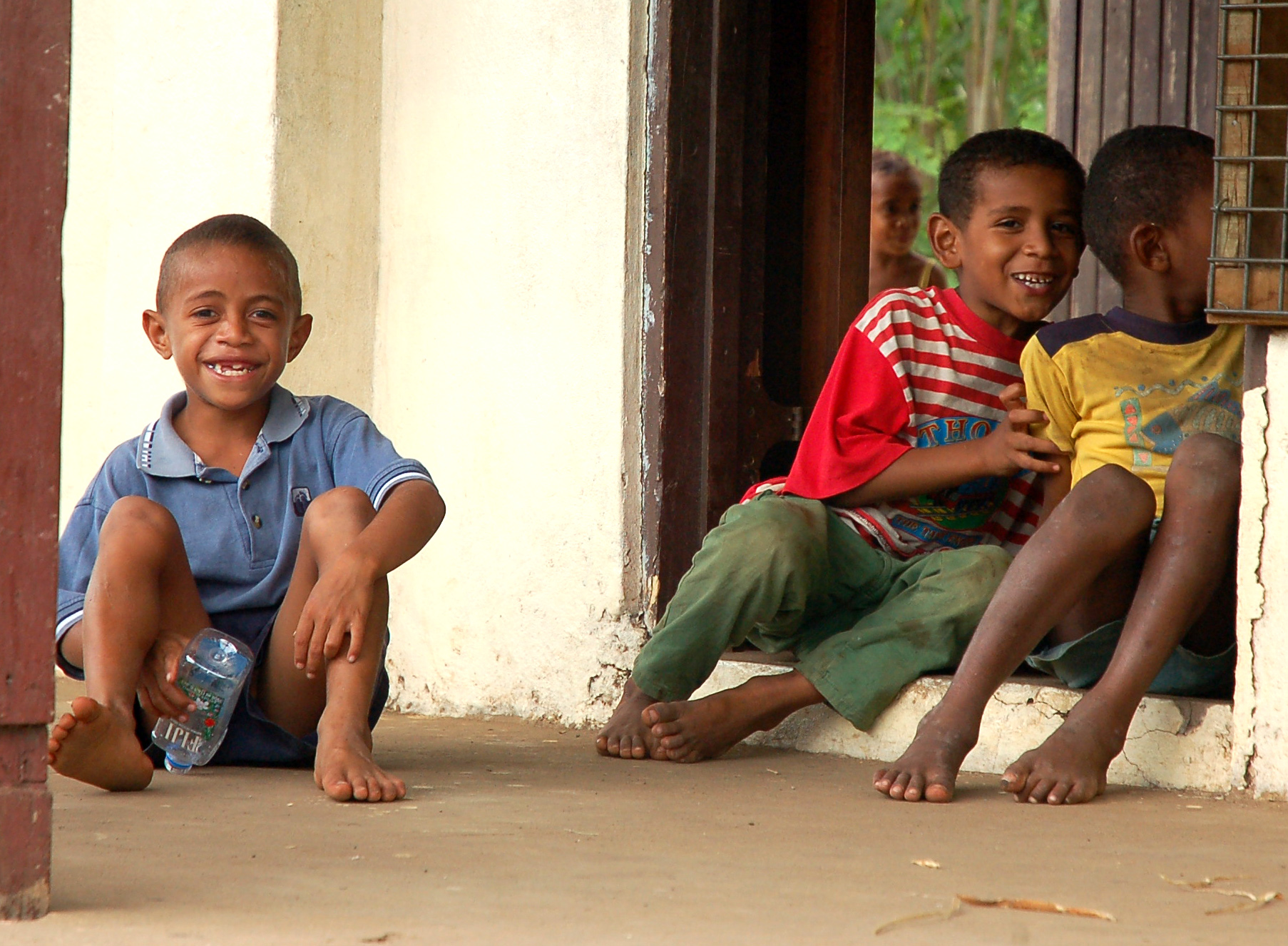 three small boys sit on the porch with their legs crossed