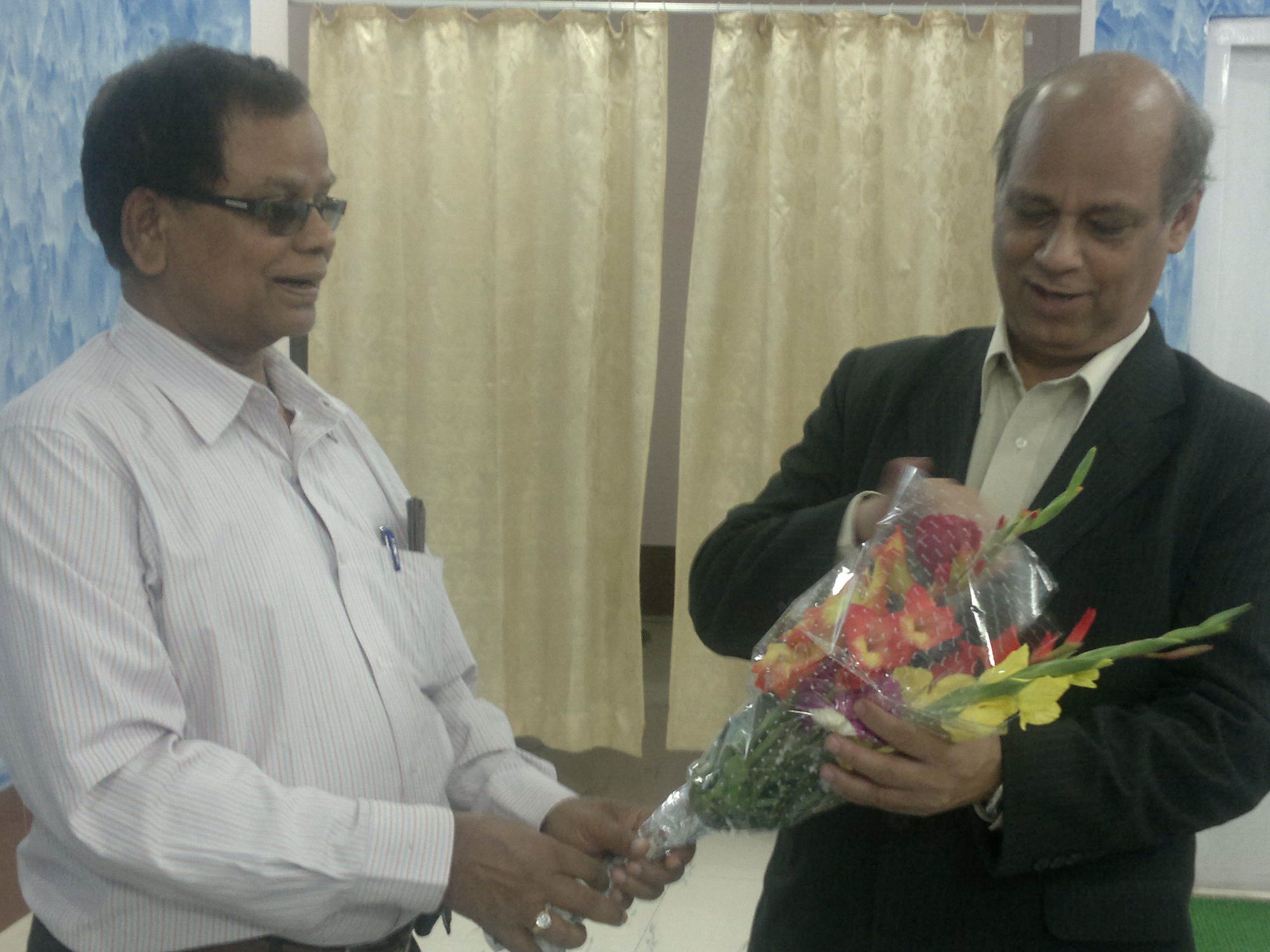 two men looking at soing in one hand and the other is wearing sunglasses and a black jacket and holding a bunch of colorful flowers