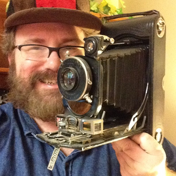 a bearded man is holding up an old fashioned camera