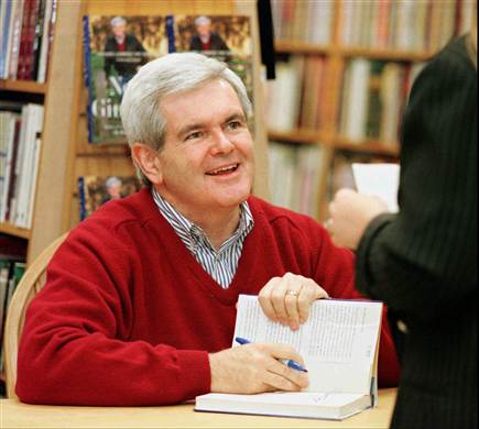 an older man with gray hair wearing a red sweater, sitting at a liry table and signing a book