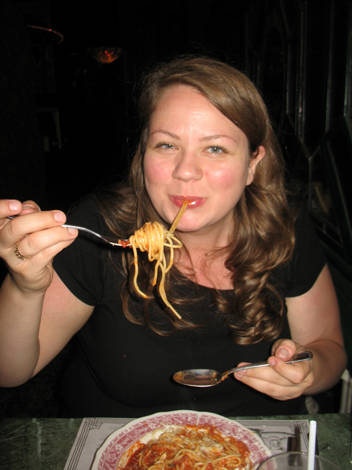 woman sitting at table eating spaghetti with fork