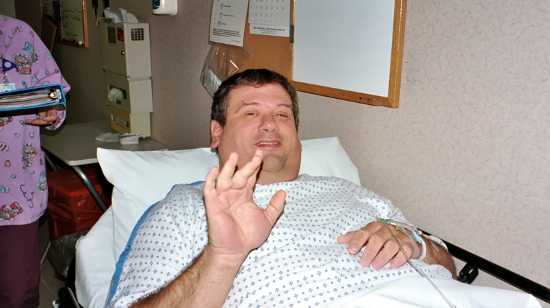 the man in hospital gown holds his hand up to his mouth