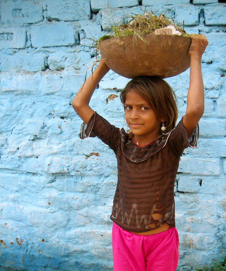 a little girl carrying a bowl on her head