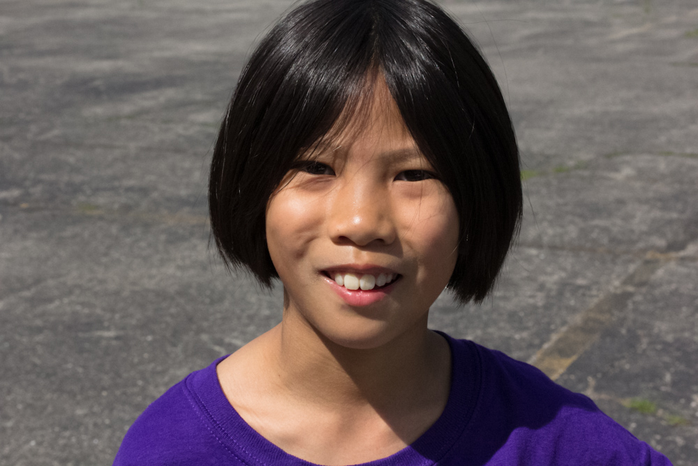 a young asian child smiling in front of a parking lot