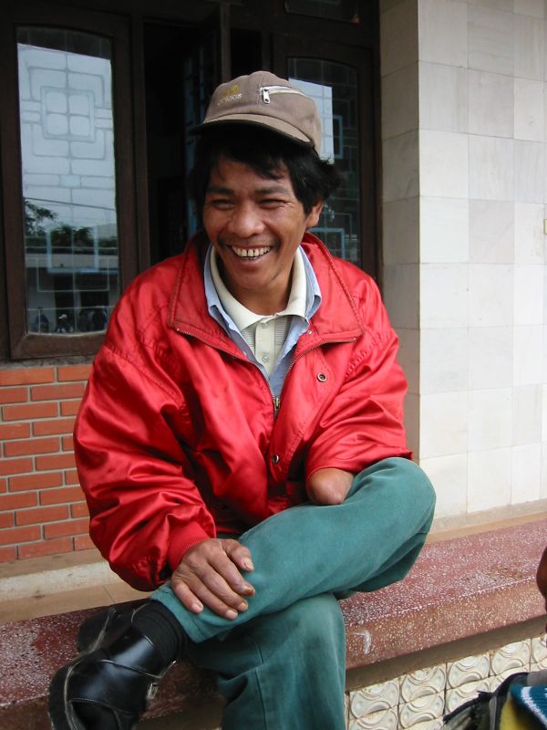 an asian man in red coat and cap sitting next to a building