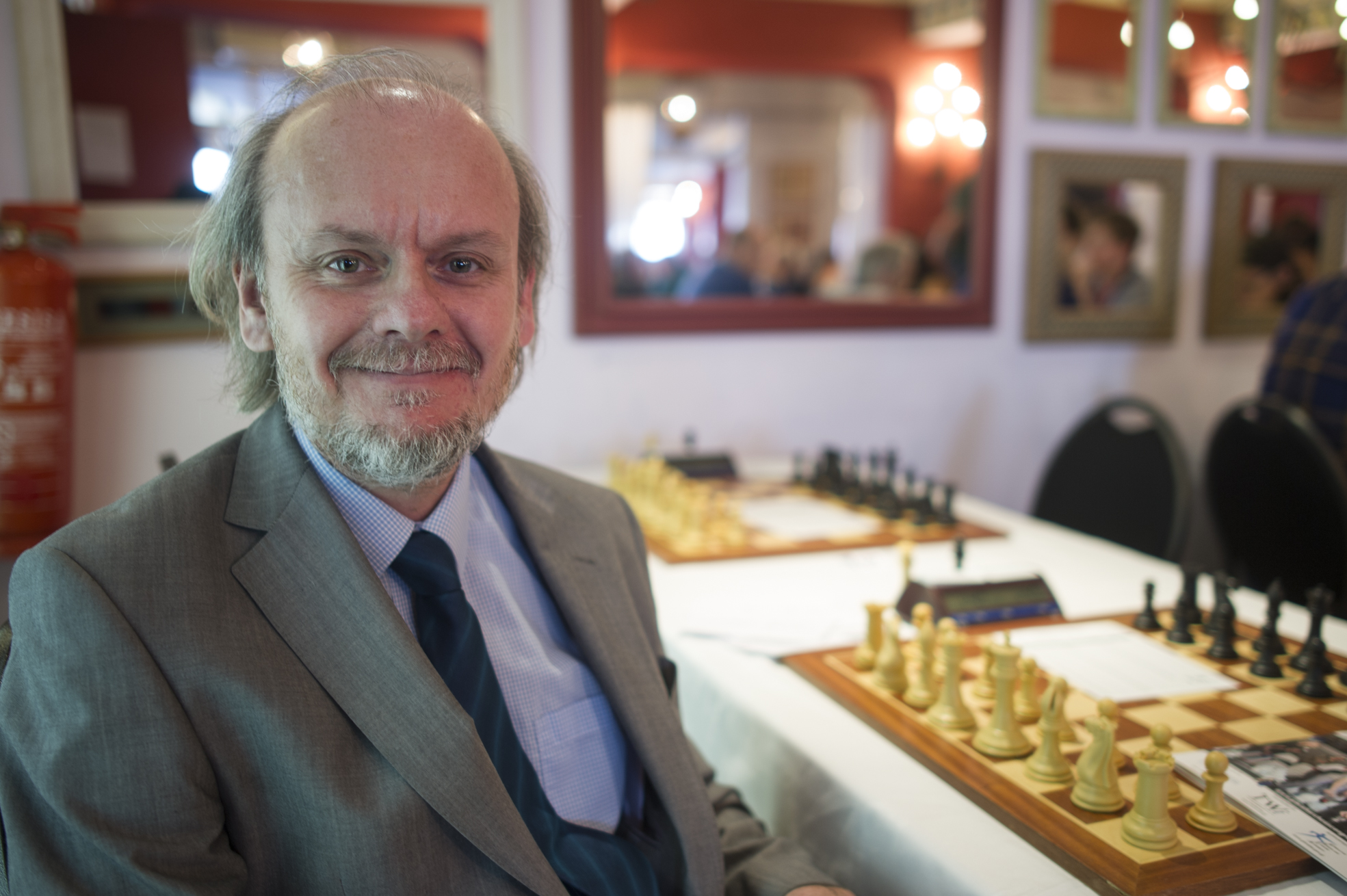 a man smiles as he poses next to a chess board