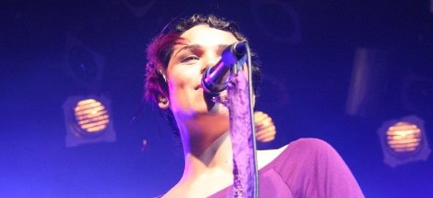 woman in purple shirt and pink pants on stage holding microphone