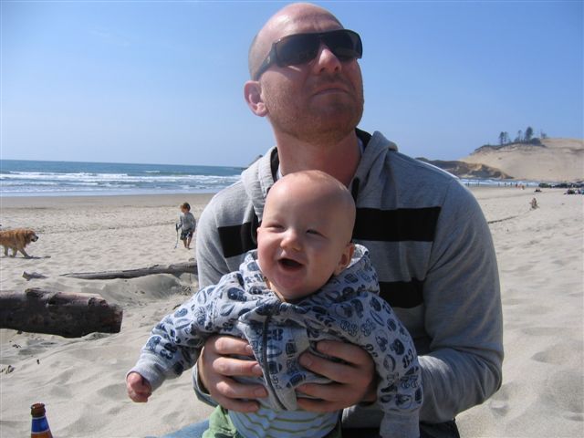the man is sitting down on the beach and holding a baby