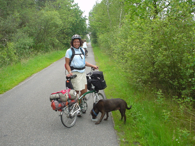 a woman on a bicycle with her dog looking at the ground