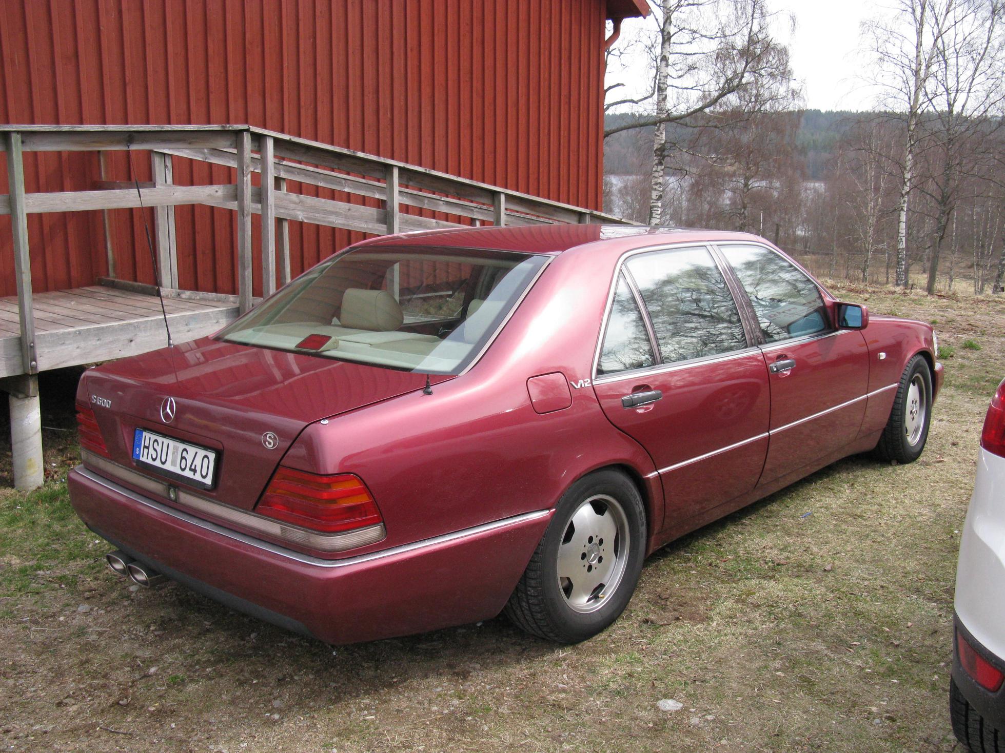 a maroon mercedes cl - type car is parked next to a red barn