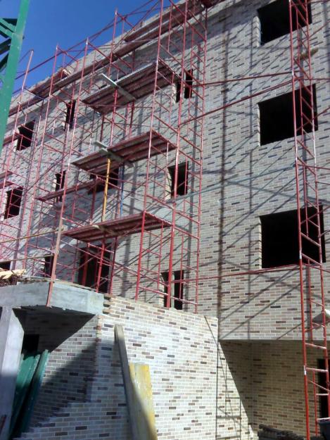 a building under construction with scaffolding and construction workers on the sidewalk