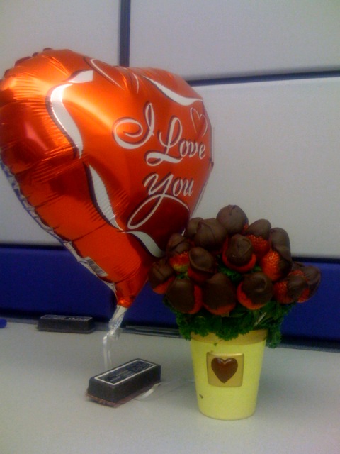 some balloons, a vase with flowers and a cell phone on a desk