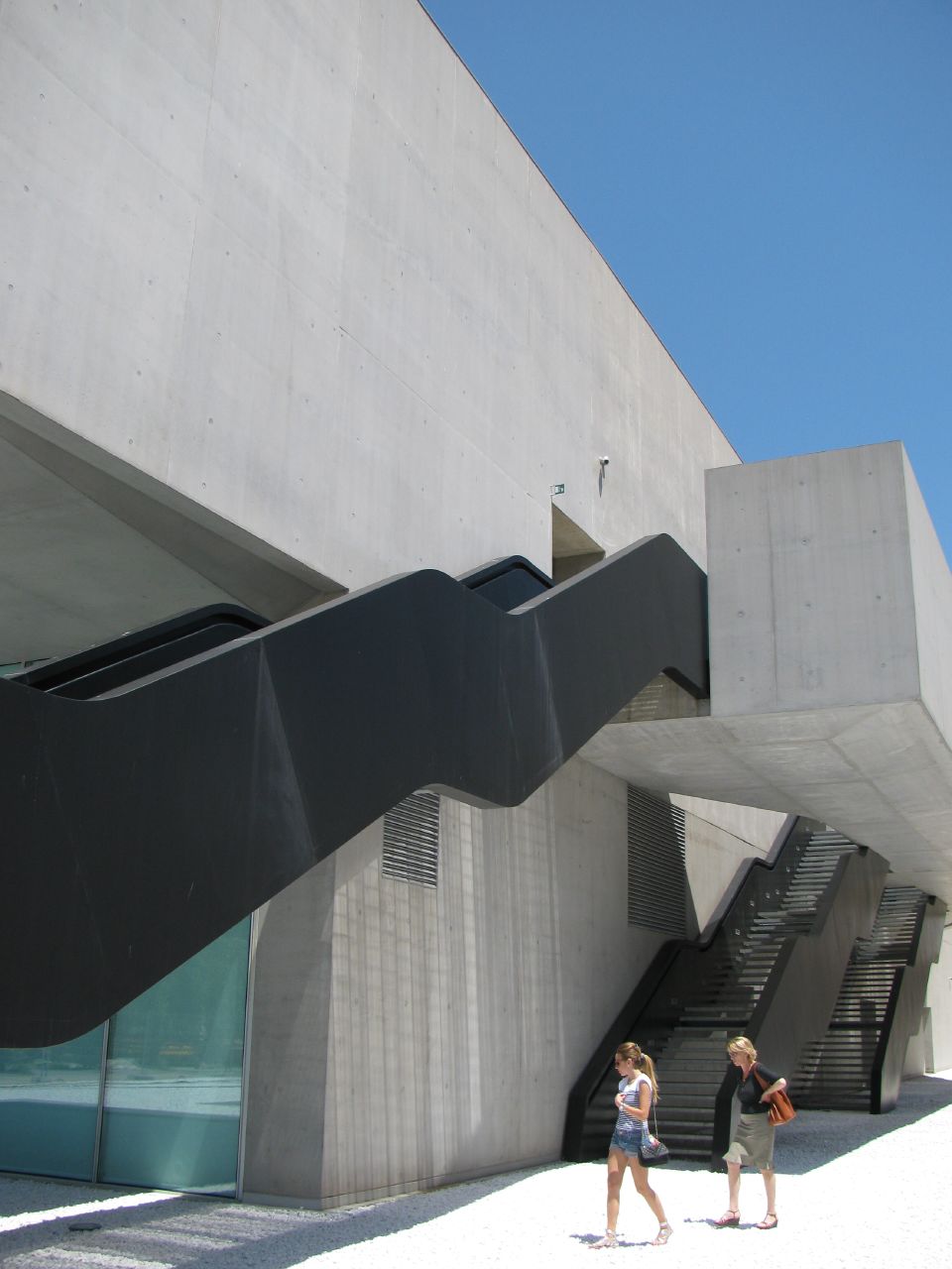 two people walking past a tall building with an open stair railing