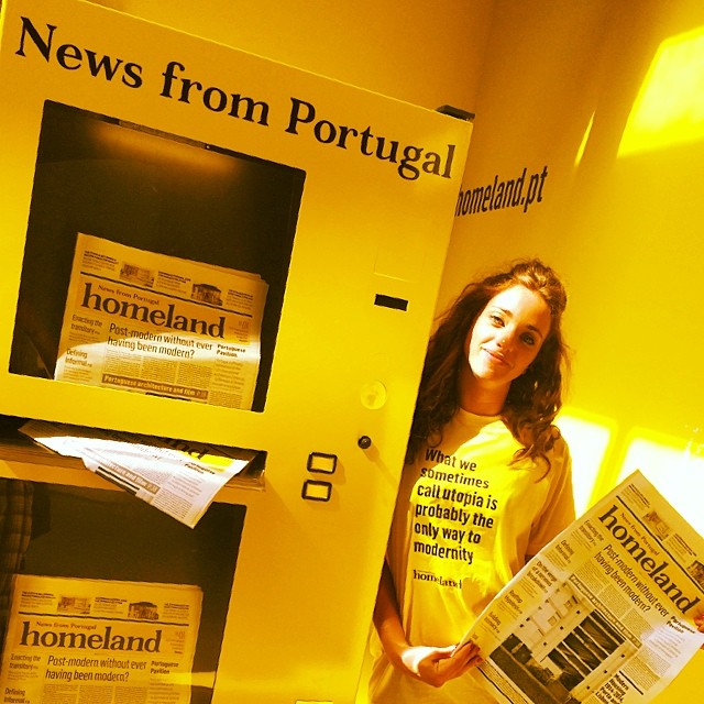 a woman standing in front of a mail box holding a newspaper