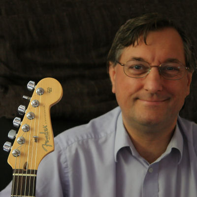 a man smiling while holding a guitar neck