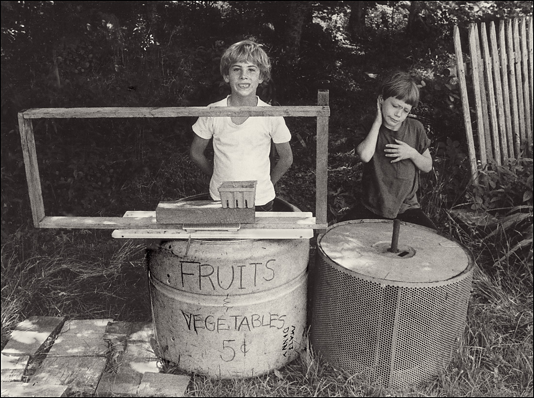 two little boys standing near a metal trash can