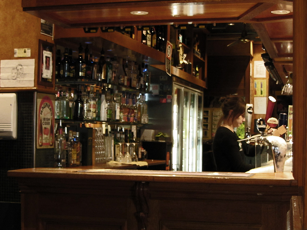 a woman behind the bar in front of bottles of liquor