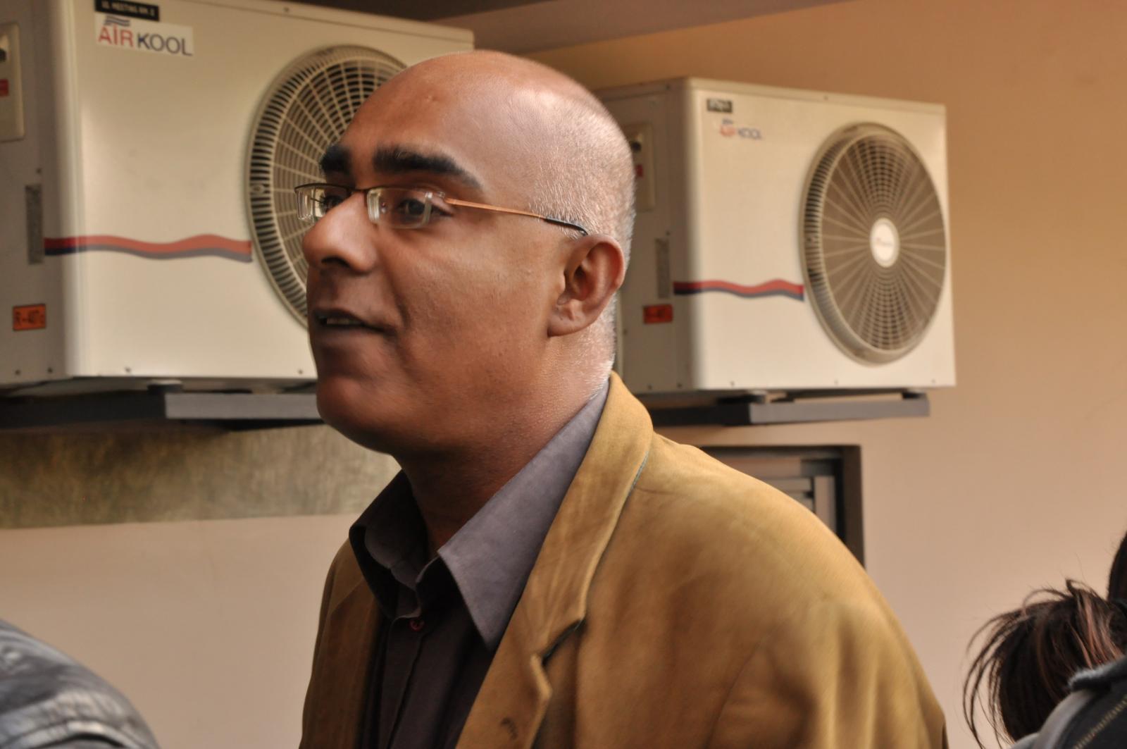 an older man in glasses and brown jacket near air conditioning units