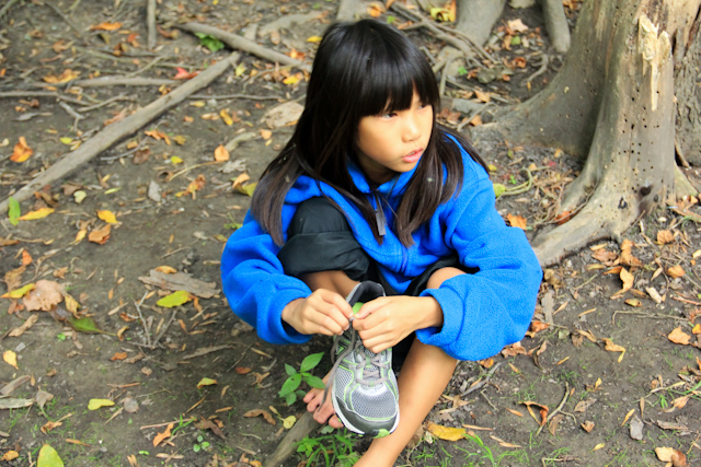 the girl is sitting in the forest with a blue jacket