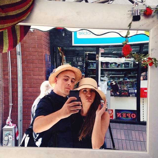 man and woman take selfie in mirror with red rose bush