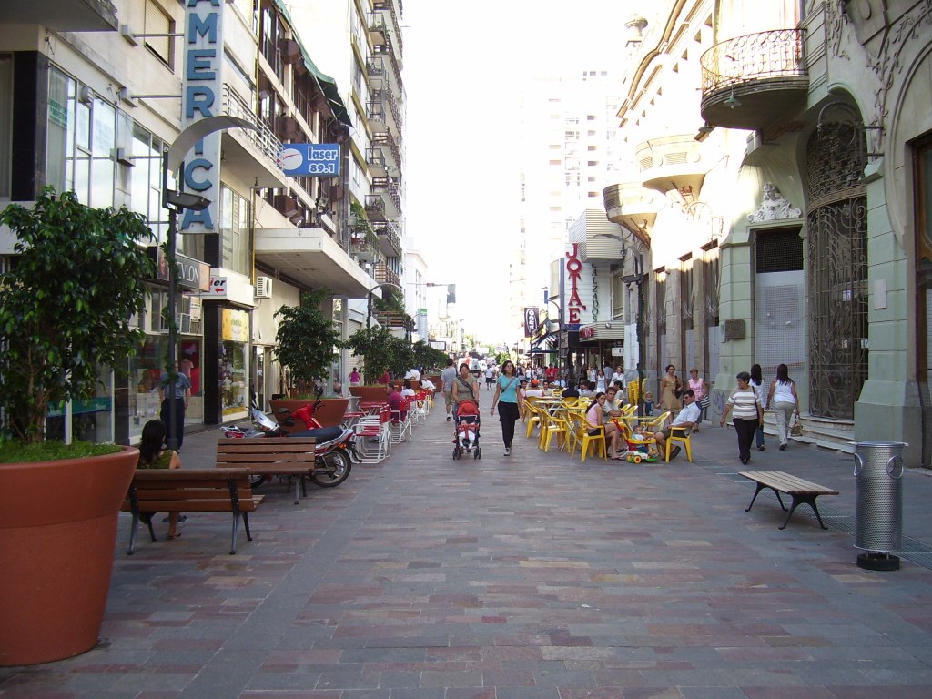 a city street with people walking on it and many parked cars on the road