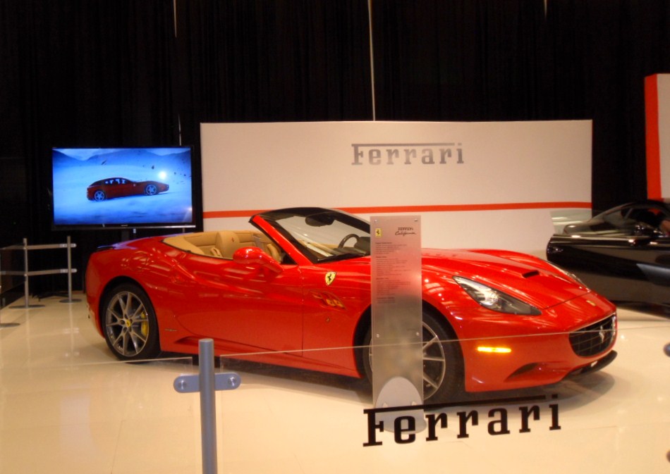 an orange sports car on display with a television in the back