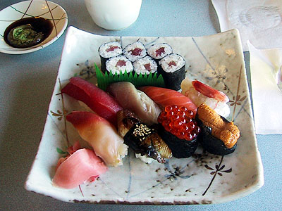 a square plate topped with sushi next to two cups of coffee