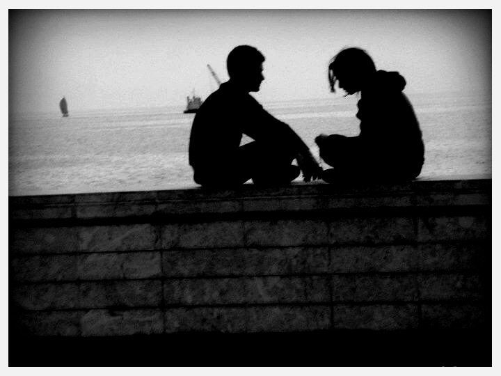 two people sitting by water looking at the water