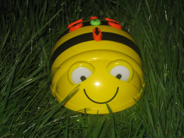a yellow helmet laying in grass that has a little bee on top